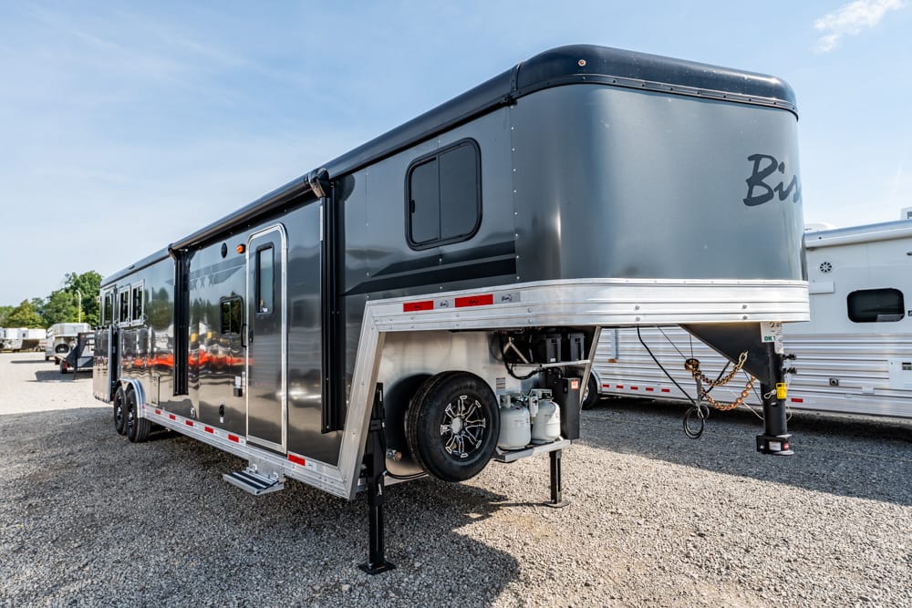 Grey fifth-wheel RV trailer on a gravel lot, front hitch and stabilizing jacks deployed, ready for towing