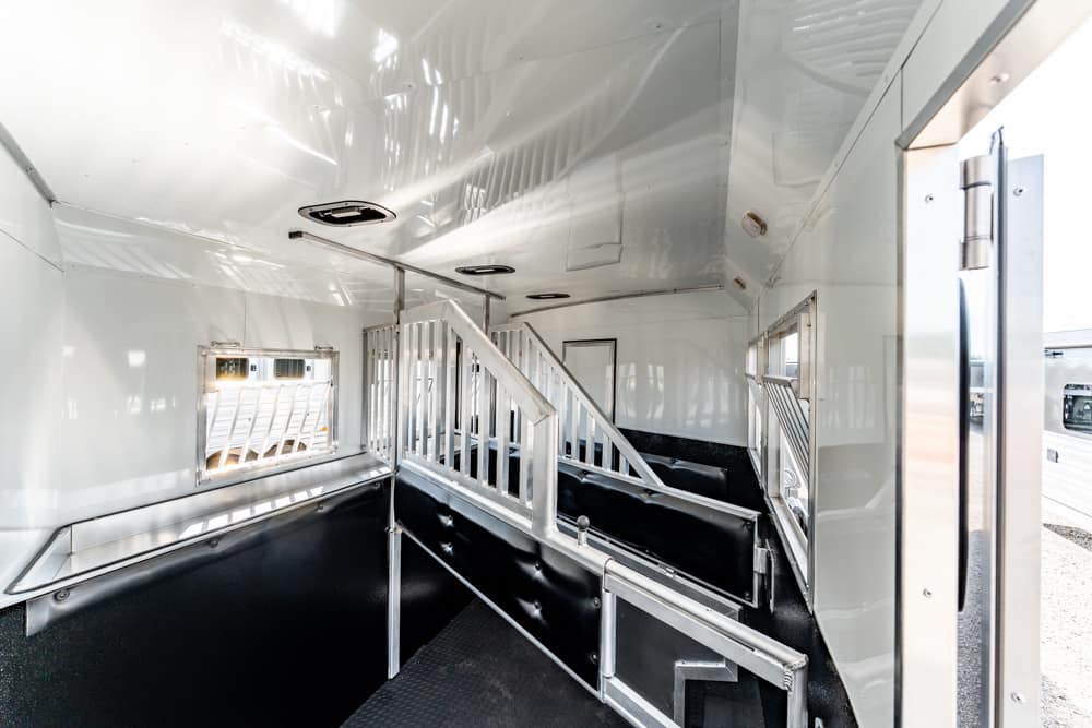 Interior of a metal livestock trailer with black cushioned stalls and a central staircase dividing the space