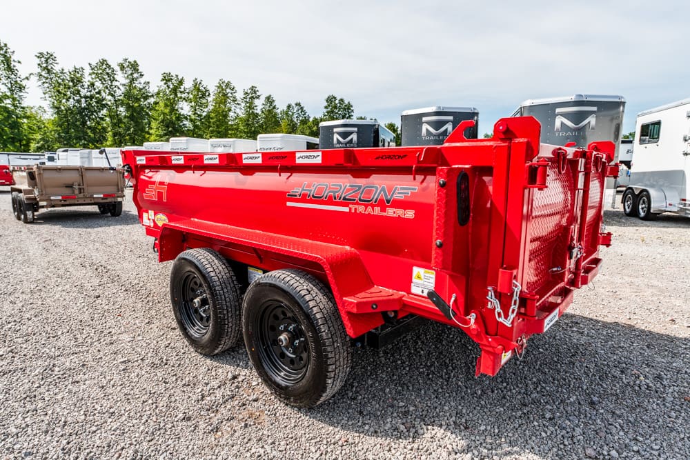 Red Horizon dump trailer with dual axles on a gravel lot, with other trailers in the background.