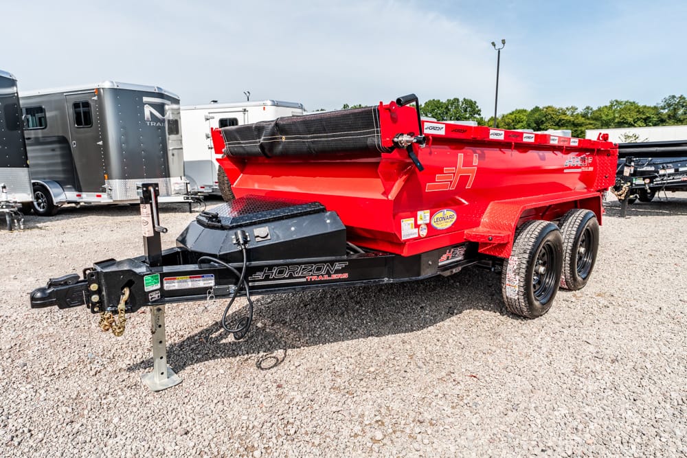 Red Horizon double-axle trailer with a rolled tarp on top, hitched to a black A-frame with a gravel lot in background.
