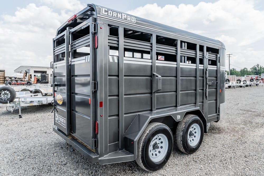 Rear three-quarter view of a gray dual-axle livestock trailer on a gravel lot, with 'Corn Pro' branding on top edge.