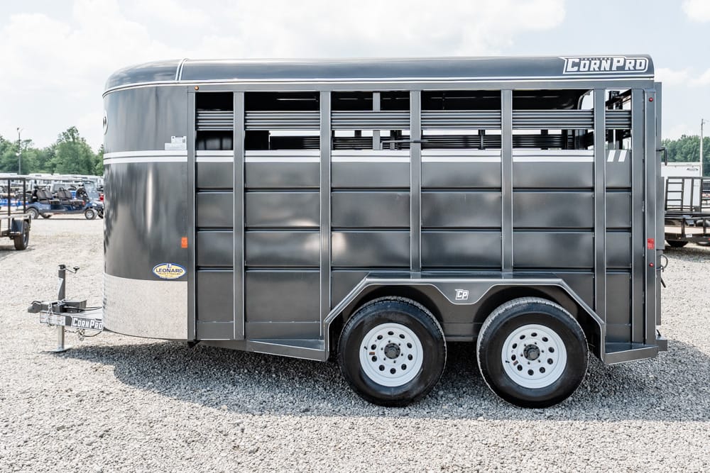 Dark gray, two‑axle CornPro livestock trailer with a front hitch, parked on a gravel lot.