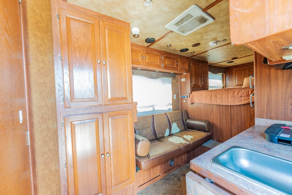 Wood-paneled RV interior with tall cabinets, a brown sofa, and a bunk bed over a kitchenette area.