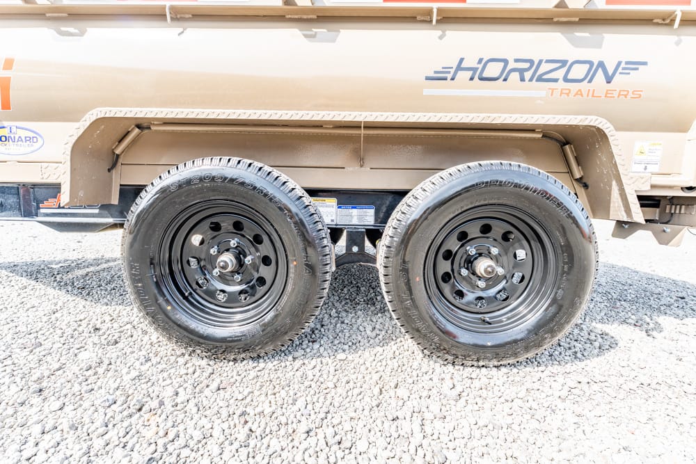 Dual black trailer wheels on a beige Horizon Trailers trailer, parked on gravel.