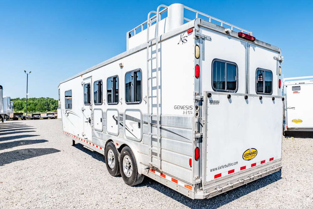 White Genesis horse trailer with two axles parked on a gravel lot; ladder on top and multiple side windows.
