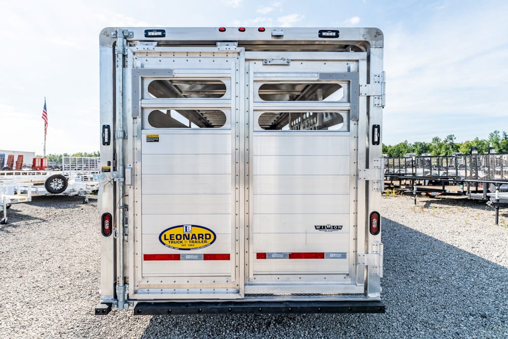 Rear view of a silver livestock trailer with two doors and a Leonard logo on a gravel lot.