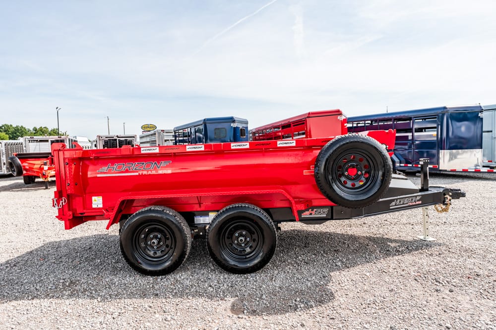 Red Horizon dump trailer on a dual-axle hitch with spare tire mounted on the side, in a gravel lot with other trailers in the background.