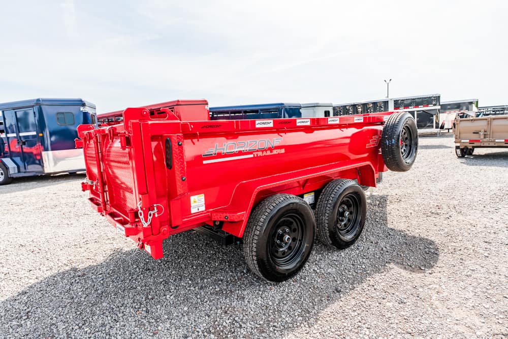 Red Horizons triple-axle dump trailer on a gravel lot, with a spare wheel mounted on the side and other trailers in the background