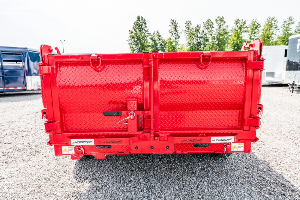 Red metal dump trailer with diamond-plate back doors closed in a gravel lot, other trailers in the background