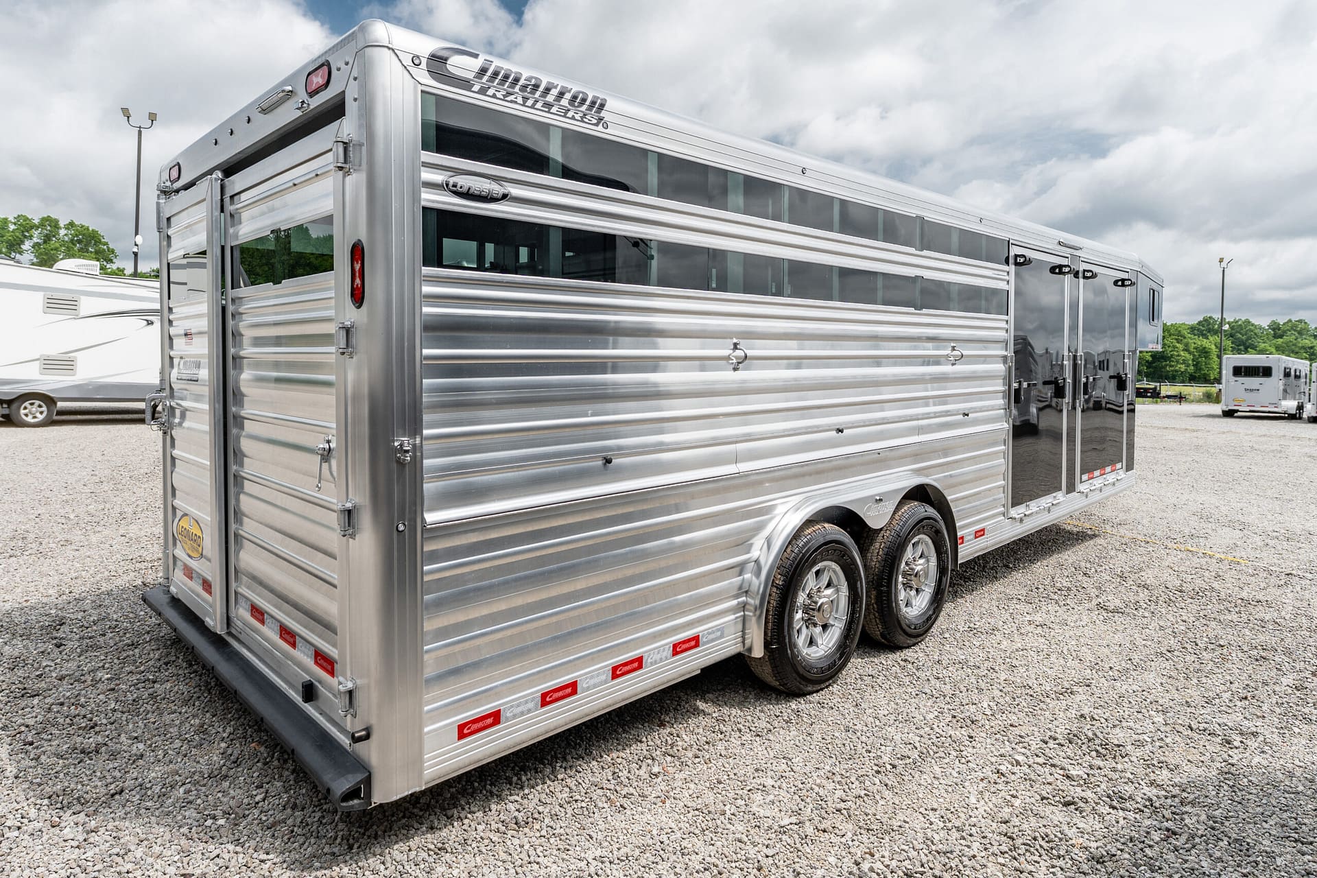 Silver aluminum enclosed trailer with multiple side doors on a gravel lot.