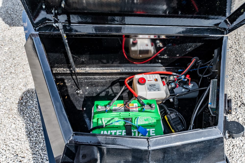 Open battery compartment of a portable generator, showing a green Interstate battery with red and black cables.