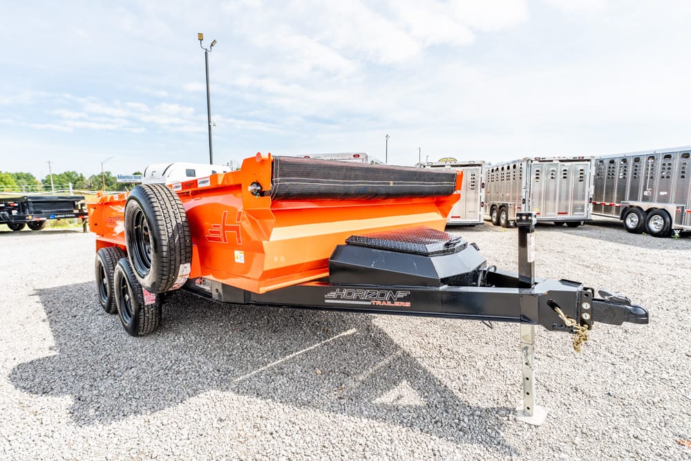 Orange Horizon dump trailer on a gravel lot, with a spare tire on the side and a black hitch in front, surrounded by other trailers.