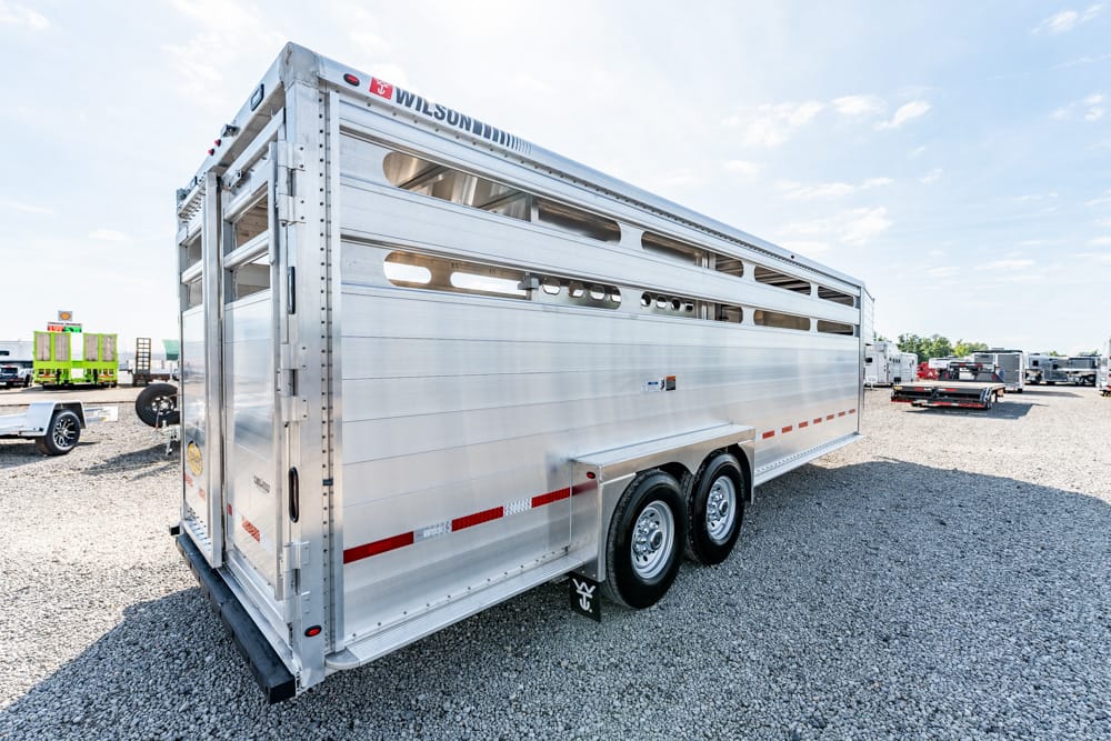 Large silver aluminum livestock trailer with ventilation slots and dual axles parked on a gravel lot.