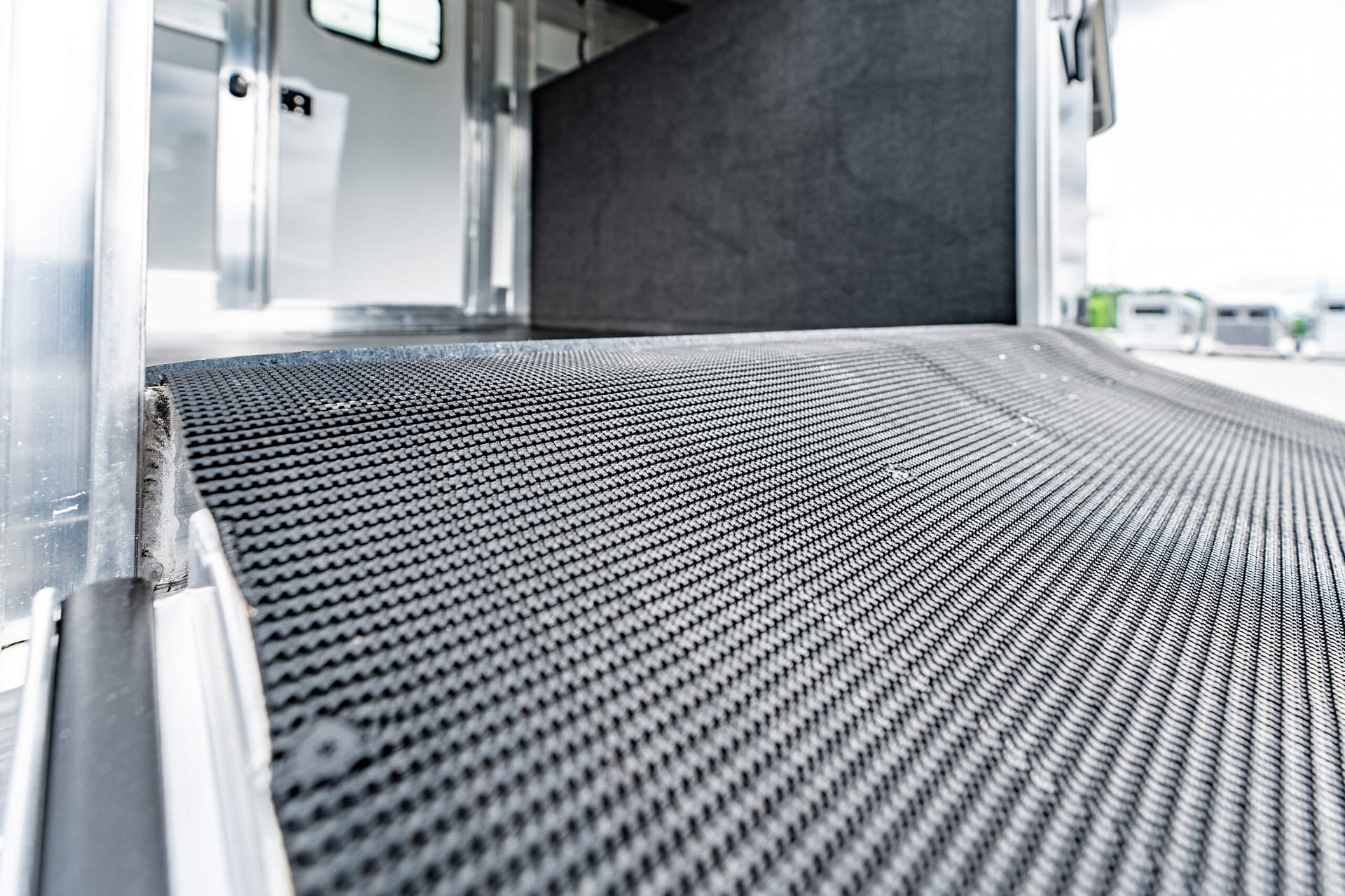 Low-angle close-up of a black, textured conveyor belt with metal rails in an industrial loading area backdrop.