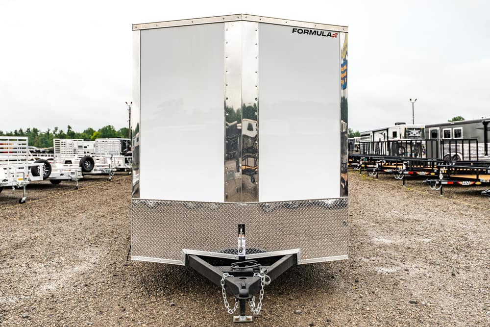 Front view of a shiny enclosed trailer on a gravel lot, hitch and safety chains visible.