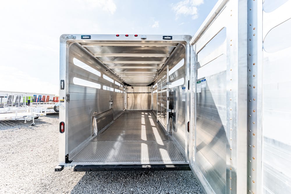 Interior of an empty aluminum cargo trailer with ribbed metal walls and diamond-plate floor, viewed from the rear opening