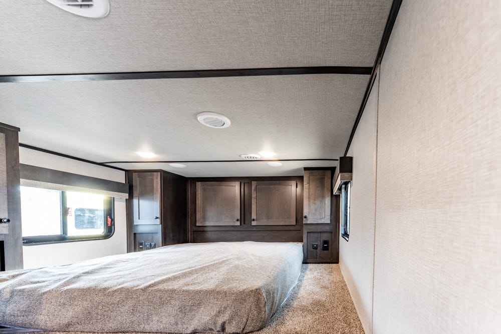 Interior of an RV bedroom with a large bed, dark wood cabinets, and beige walls.