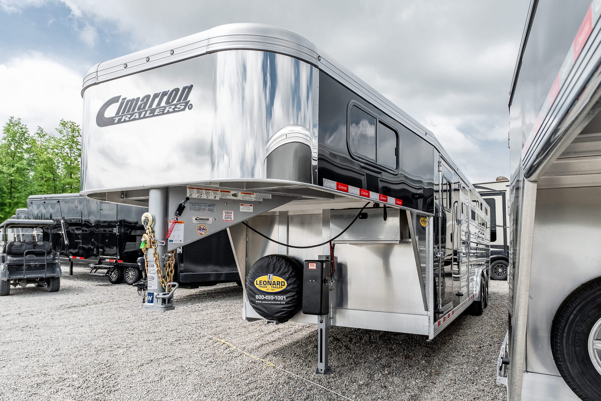 Silver gooseneck trailer with Cimarron Trailers branding in a row of trailers on a gravel lot.