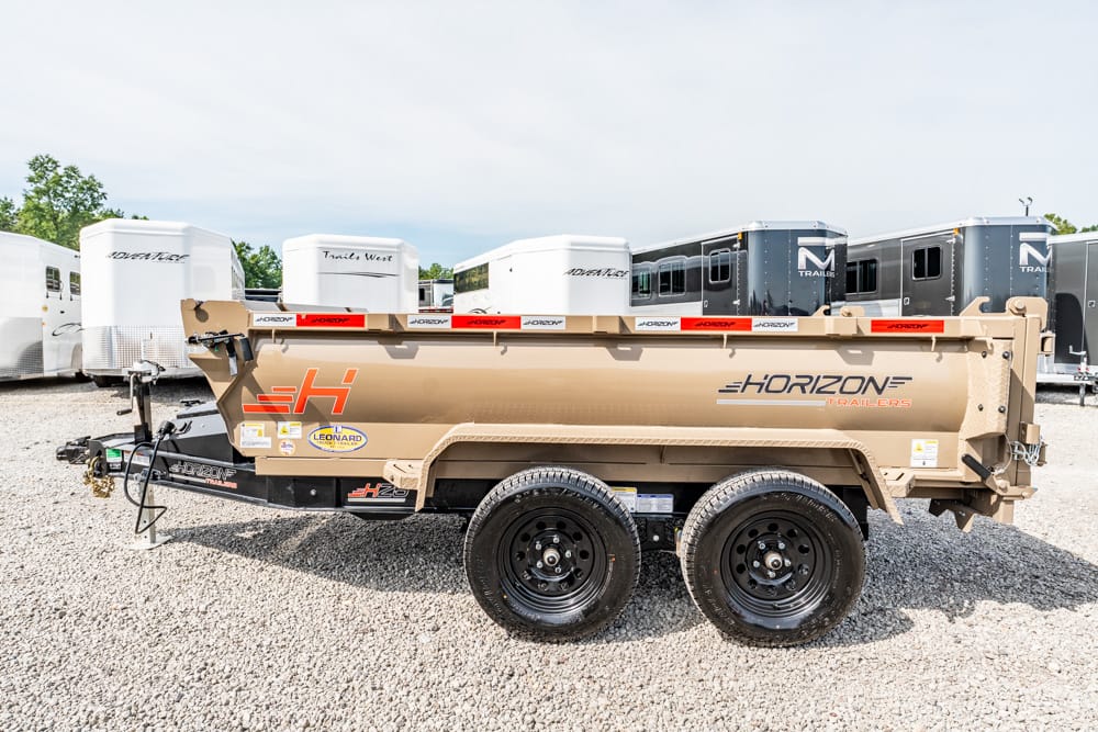 Tan Horizon dump trailer on a gravel lot with dual axles and black wheels, logo visible on side, horse trailers in background.
