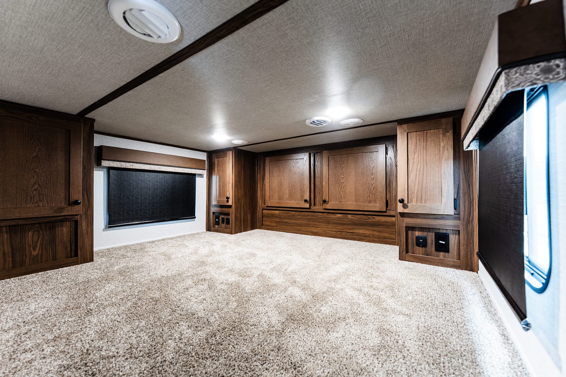 Wood-paneled RV living area with upper and lower cabinets, beige carpet, and round ceiling lights.