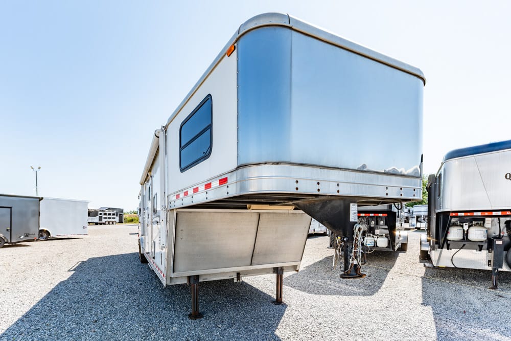White fifth-wheel RV trailer raised on its front landing gear in a gravel lot with other trailers nearby under a clear sky, daytime