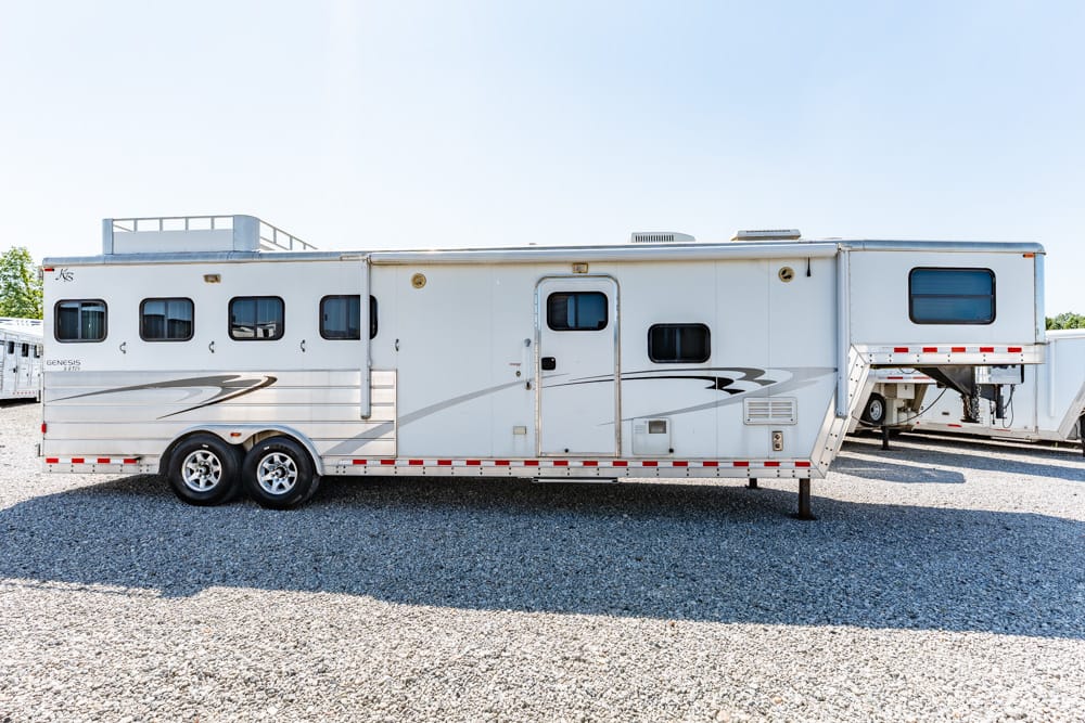 White long travel trailer with multiple windows parked on gravel.