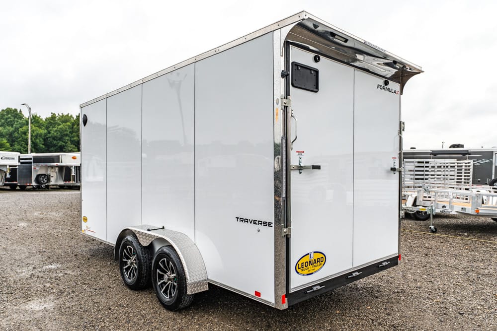 White tandem-axle enclosed cargo trailer with back doors, parked on a gravel lot (Leonard logo visible).