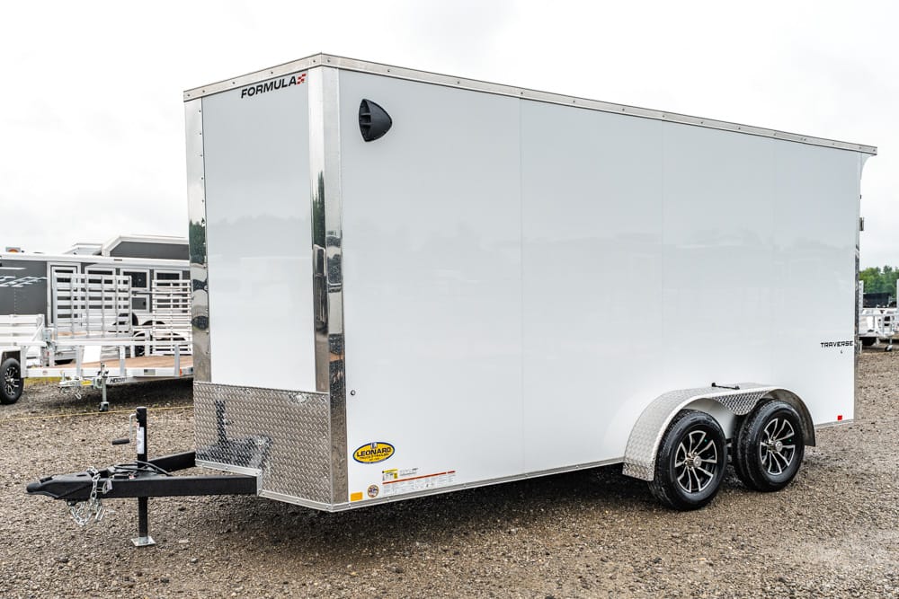 White enclosed tandem-axle cargo trailer on a gravel lot, with a hitch at the front and diamond-plate tongue.