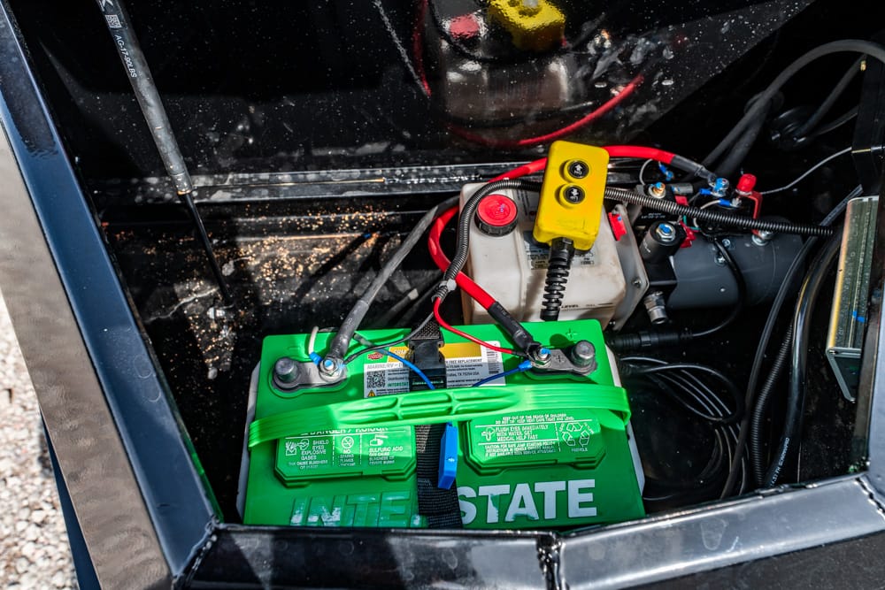 Green Interstate battery with connected red/black cables inside a metal enclosure; a yellow safety switch/module rests on top.