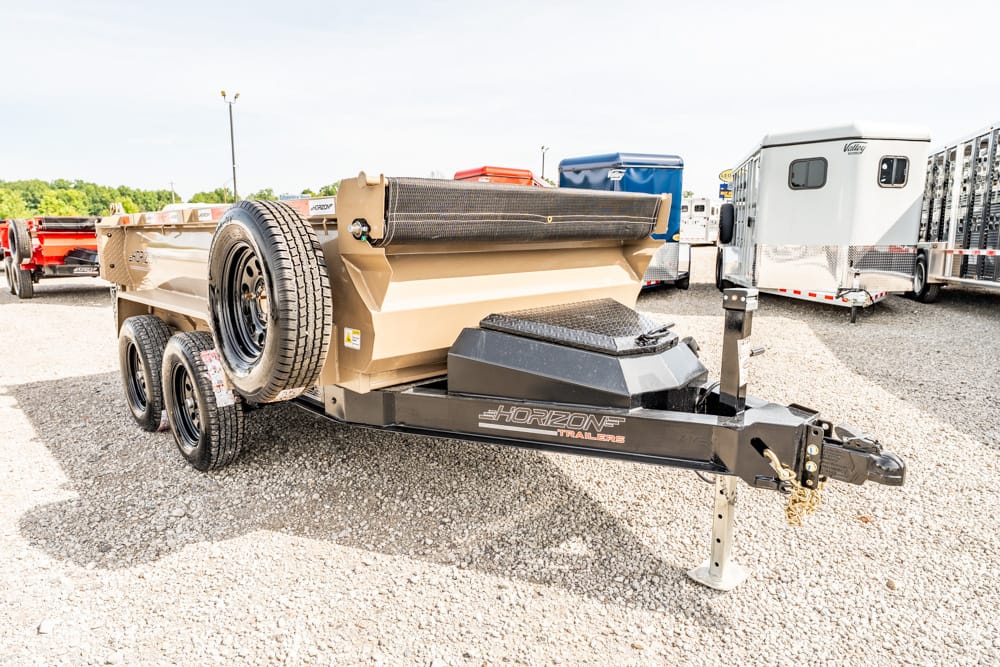 Dual-axle trailer with beige bed and mounted spare tire on a gravel lot, Horizon Trailers branding on the hitch area.