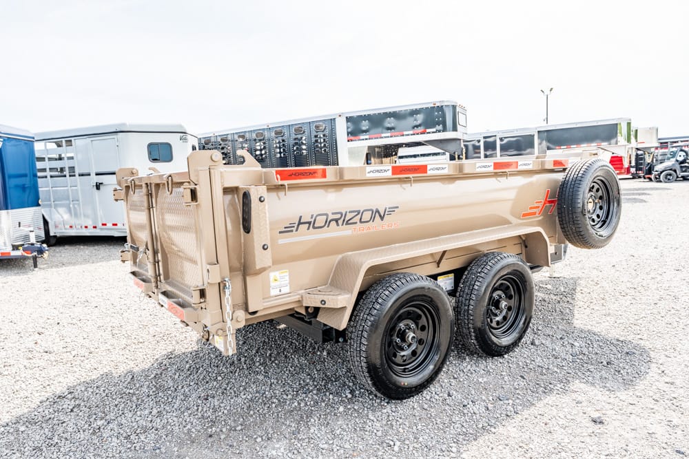 Beige Horizon dump trailer with two axles on a gravel lot, spare tire mounted on the side, with other trailers in the background.