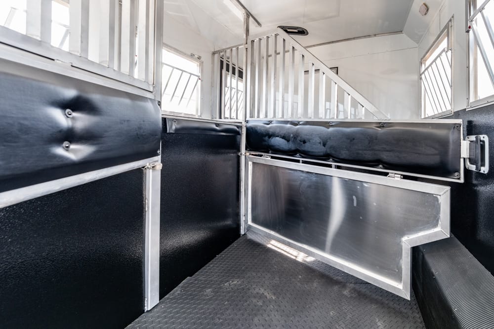 Interior of a horse trailer with metal dividers, black padded walls, and a diamond-plate floor shortly after entering from the back door