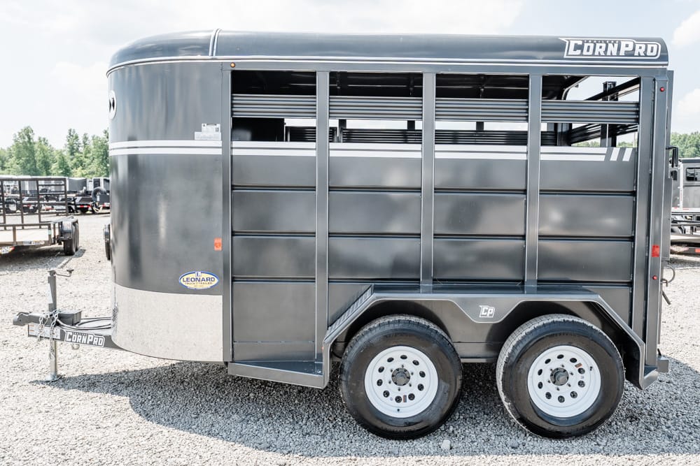 Dark gray CornPro livestock trailer with tandem axles and vented side panels on a gravel lot.