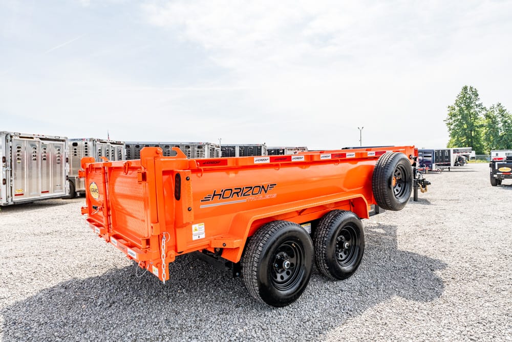 Orange Horizon dump trailer with dual rear axles parked on a gravel lot, other trailers in the background.