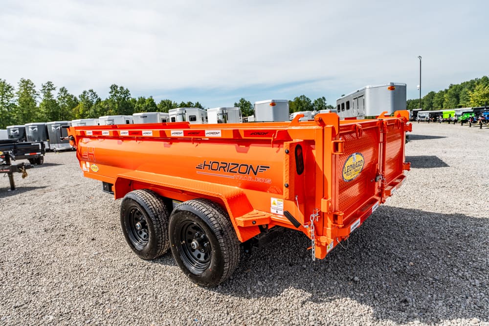 Orange Horizon dump trailer with dual axles in a gravel trailer yard, with other trailers in the background.