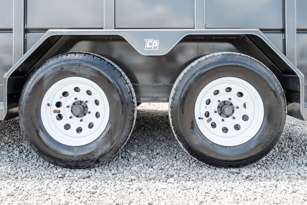 Dual-axle trailer with black fenders and white steel wheels on a gravel surface.