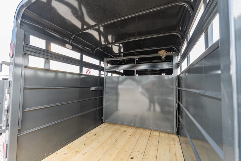 Interior of an empty dark gray trailer with a wooden floor, ribbed side walls, and a metal divider at the far end.