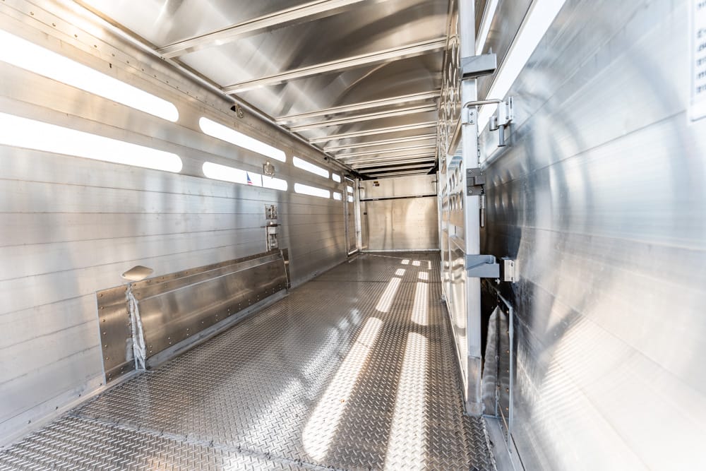 Interior of an empty aluminum trailer with diamond-plate floor and slotted side walls, bright metal surfaces casting long shadows.