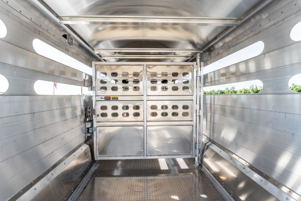 Interior of a metal livestock trailer with a perforated divider gate and ventilation slots visible on the doors and walls.