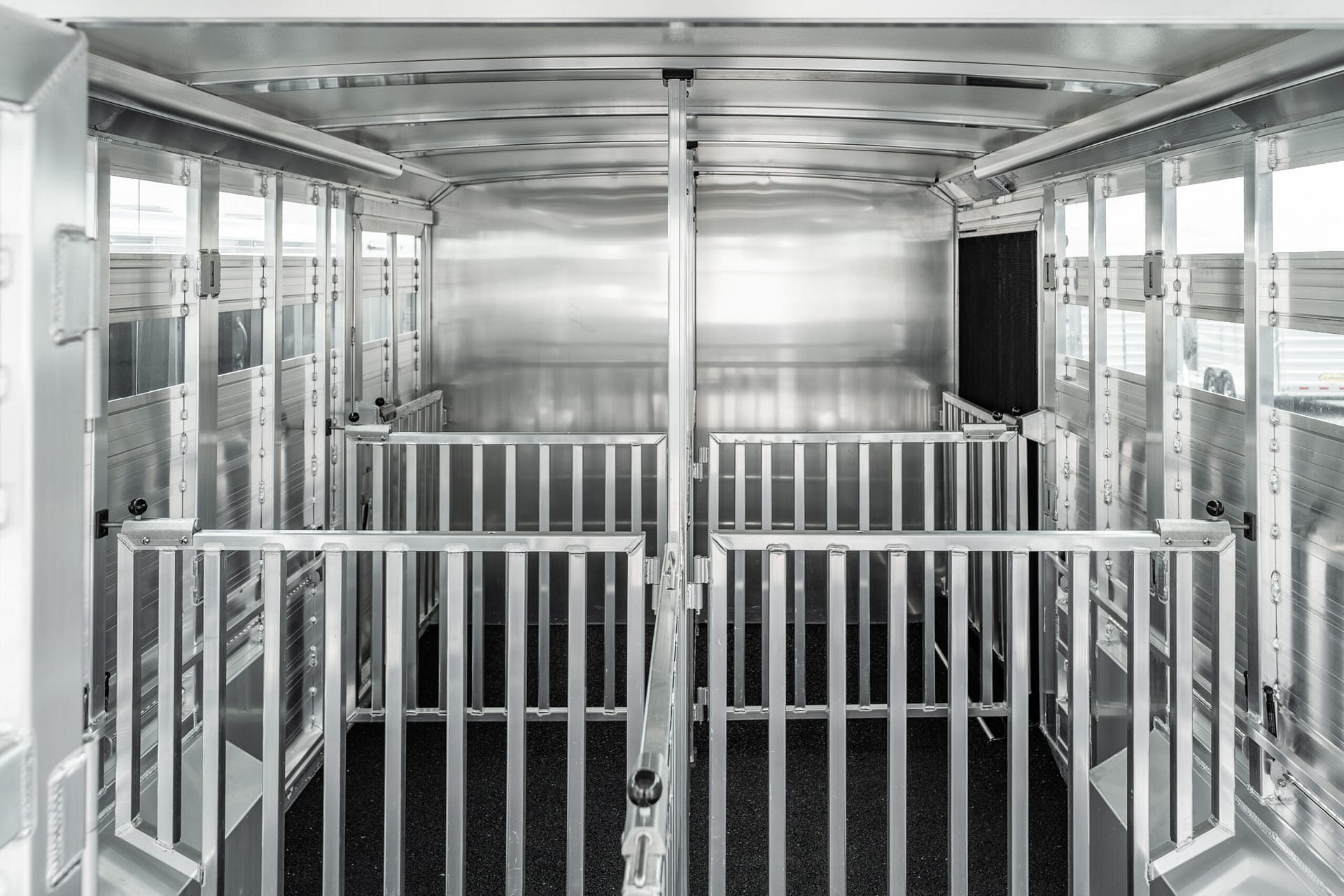 Interior of a silver aluminum trailer with metal partitions and stalls for livestock, empty and ready for loading.