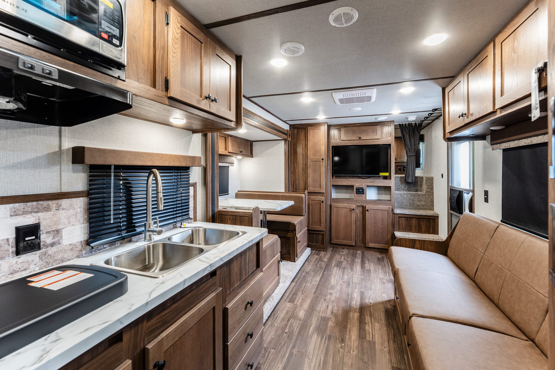 Interior of a wood-paneled RV kitchen with a double sink, marble countertop, and upper cabinets above.