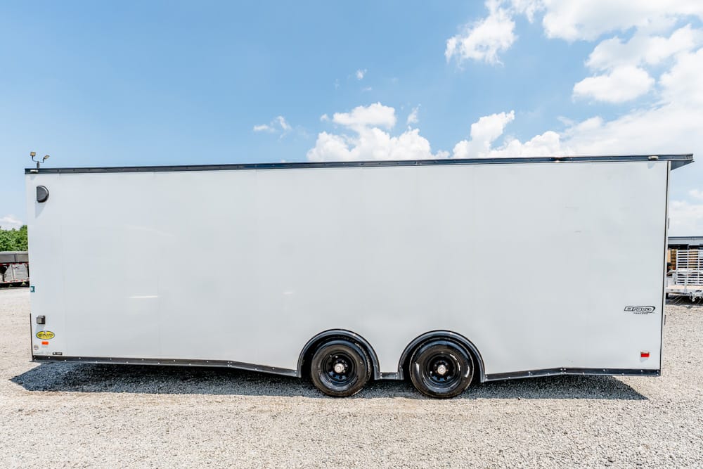 White enclosed cargo trailer with two axles on a gravel lot under a blue sky.