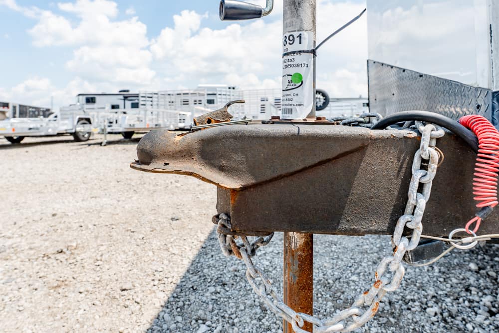Rusty trailer hitch with safety chains in a gravel lot, with trailers visible in the background.