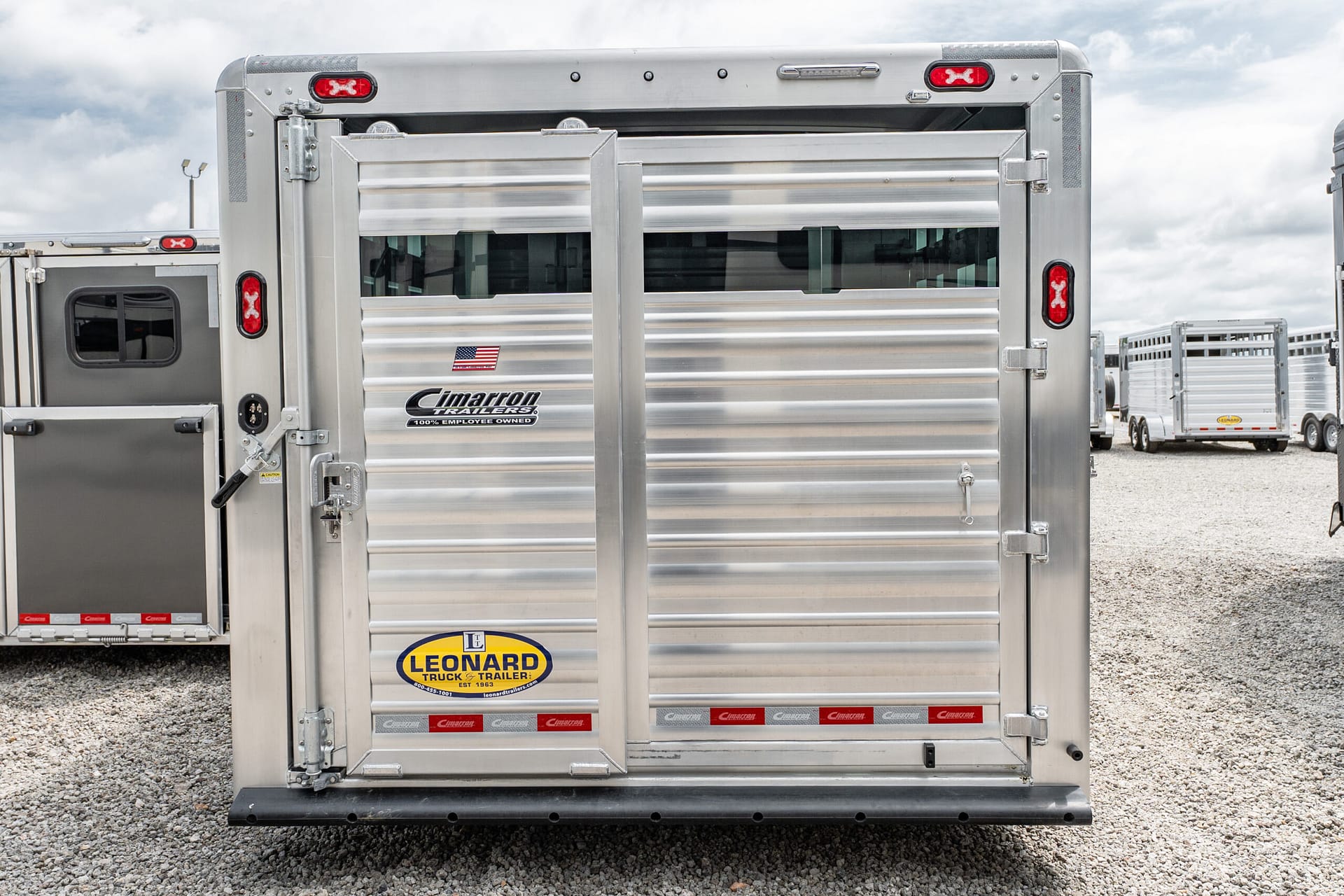 Rear view of a large aluminum trailer with closed double doors, red taillights, and a Leonard Trailers sticker.