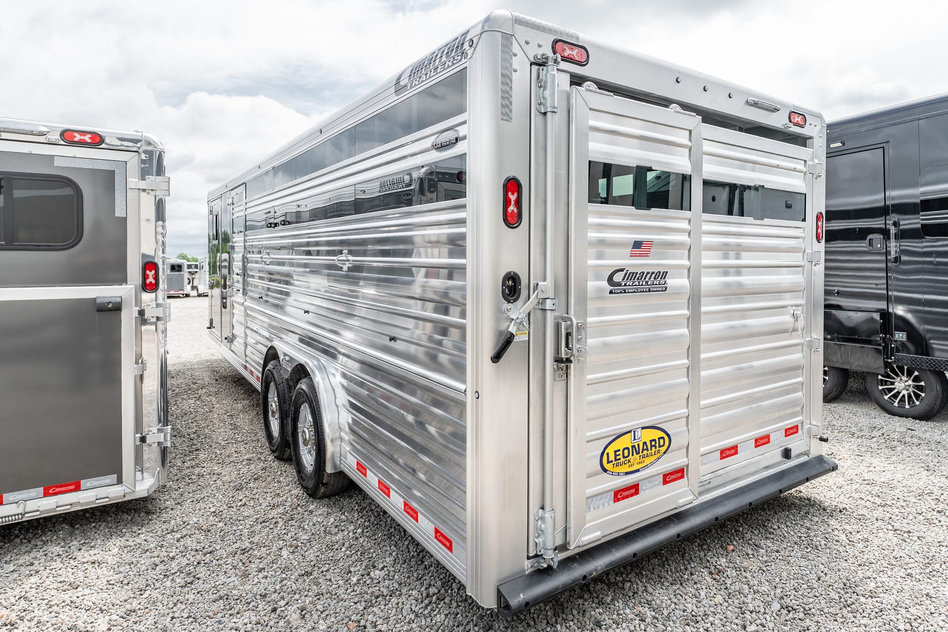 Row of shiny aluminum horse trailers parked on a gravel lot, with Cimarron and Leonard logos visible on the sides.