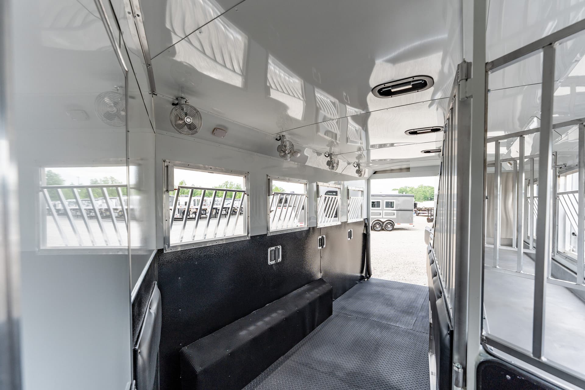 Interior of a white horse trailer with side stalls, ceiling fans, and a rubberized ramp at the bottom of the aisle