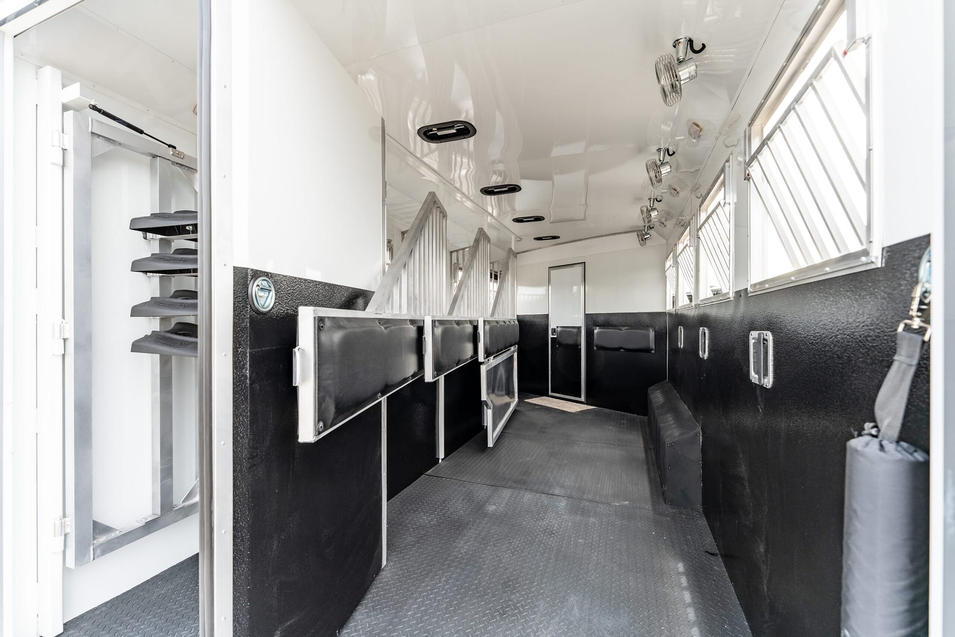 Interior of a white horse trailer with row of stalls, black padded dividers, and a non-slip patterned floor