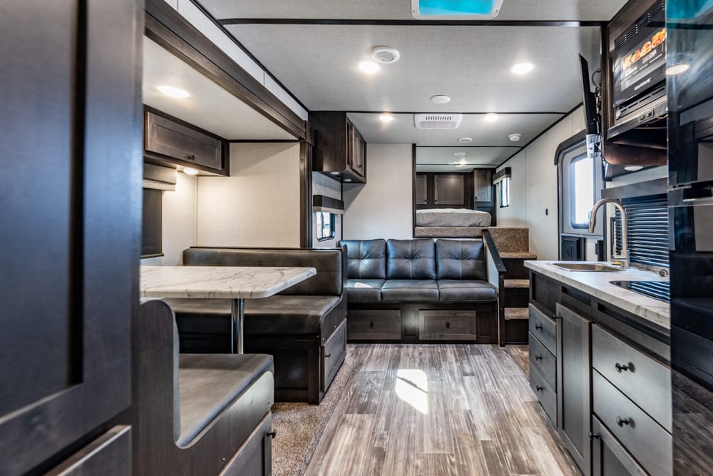 Interior of an RV with a kitchen on the right, a gray sofa, and a dining booth on the left