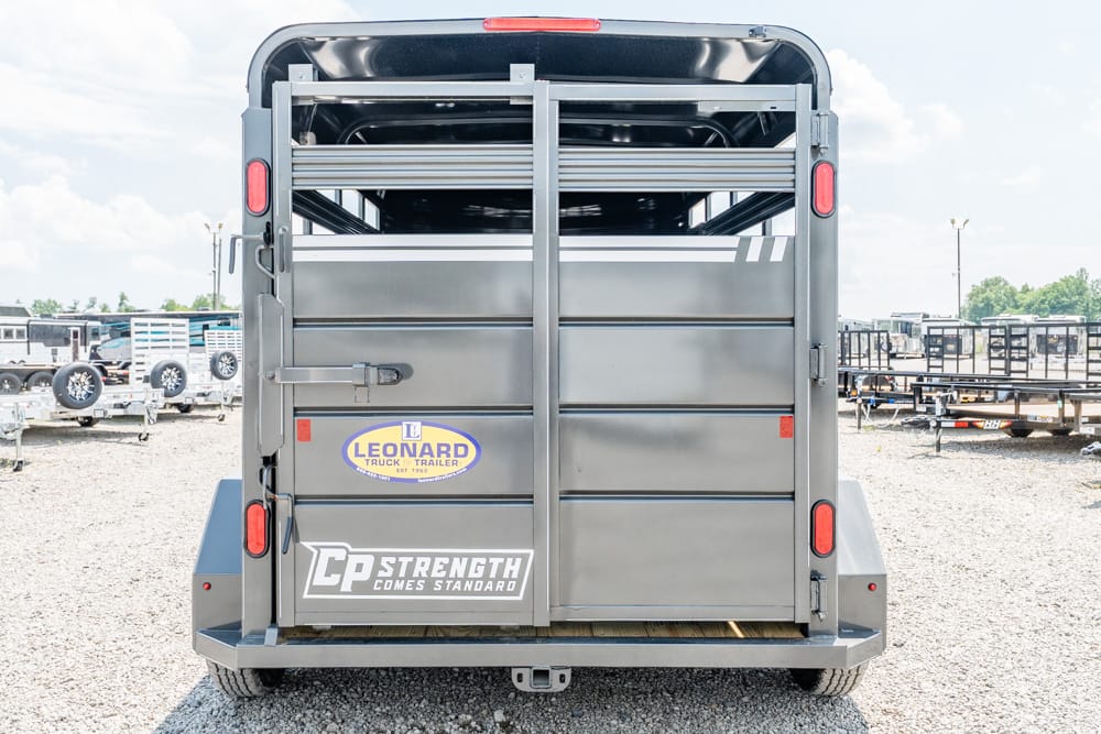 Rear view of a gray livestock trailer with double doors, red brake lights, and Leonard branding in a gravel lot