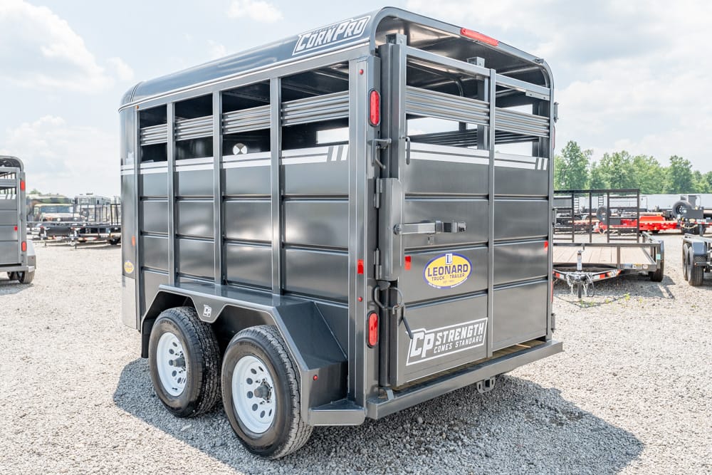 Gray, two-axle livestock trailer with open side slats parked on a gravel lot, logos visible on rear doors (Leonard, CP Strength Comes Standard)